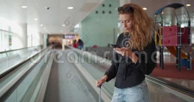 坐自动扶梯的女人，在国际机场拿着行李用手机。